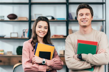 Two smiling students holding notebooks and looking at camera clipart