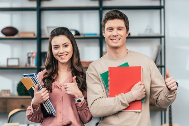 İki gülümseyen öğrenci notebooklar tutarak ve başparmak yukarı gösteren