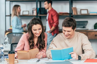 Masada oturan ve birlikte kitap okuma gülümseyen öğrenciler
