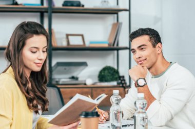 Two multiethnic students sitting at desk with books and studying together clipart