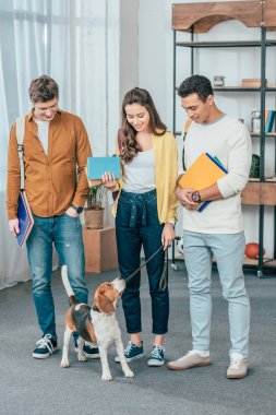 Köpek tutarak notebooklar ile üç çok etnik gülümseyen öğrencilerin tam uzunlukta görünümü
