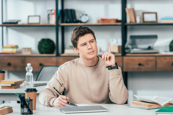 Pensive Student Sitting Table Laptop Book Pointing Finger — Stock Photo, Image