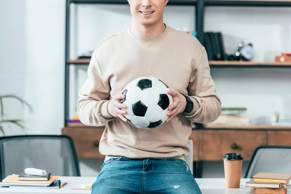 テーブルの上に座り 職場でサッカーボールを持っている笑顔の若者のクロップドビュー — ストック写真