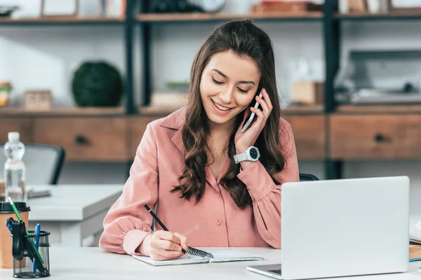 Menina Sorridente Cabelos Escuros Camisa Rosa Falando Smartphone Escrevendo Notebook — Fotografia de Stock