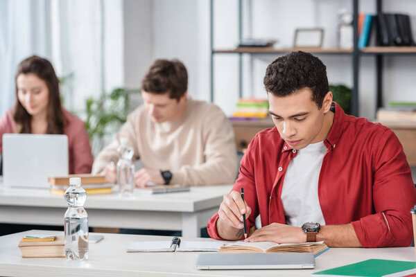 Concentrated student sitting at desk and reading book in classroom