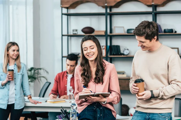 Joven Sonriente Con Taza Papel Café Mirando Chica Con Cuaderno — Foto de Stock