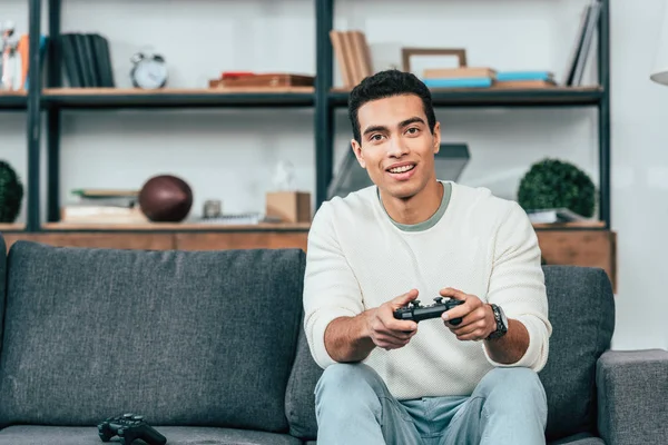 Fröhlicher Junger Mann Sitzt Auf Sofa Und Hält Gamepad — Stockfoto