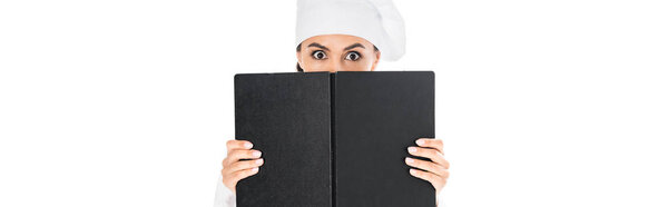 Panoramic shot of shocked chef in uniform holding black book isolated on white