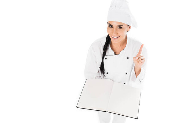 Smiling chef holding open book and showing idea gesture isolated on white