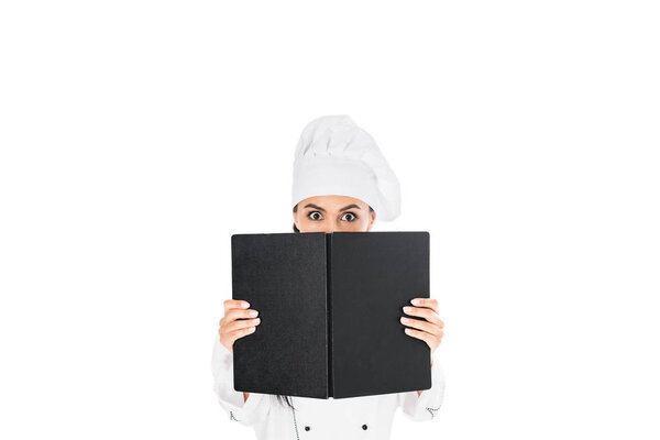 Shocked chef in uniform holding black book isolated on white