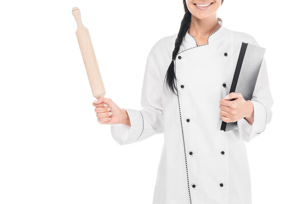 Cropped view of chef in uniform holding rolling pin and book isolated on white