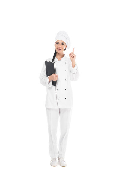 Full length view of chef in uniform holding black book and showing idea gesture isolated on white
