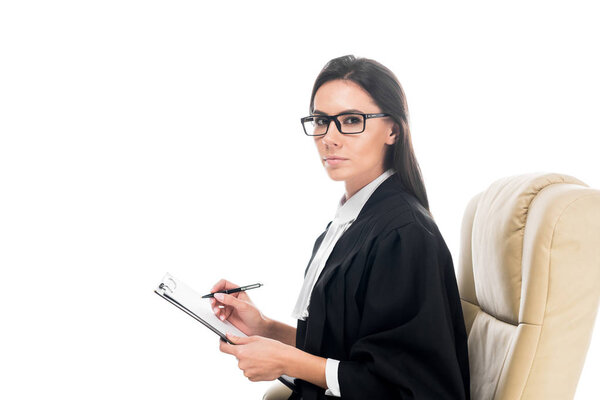 Judge sitting in armchair and writing on clipboard isolated on white