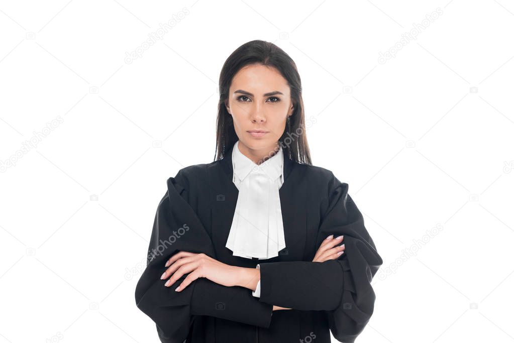 Front view of serious judge in judicial robe standing with folded arms isolated on white