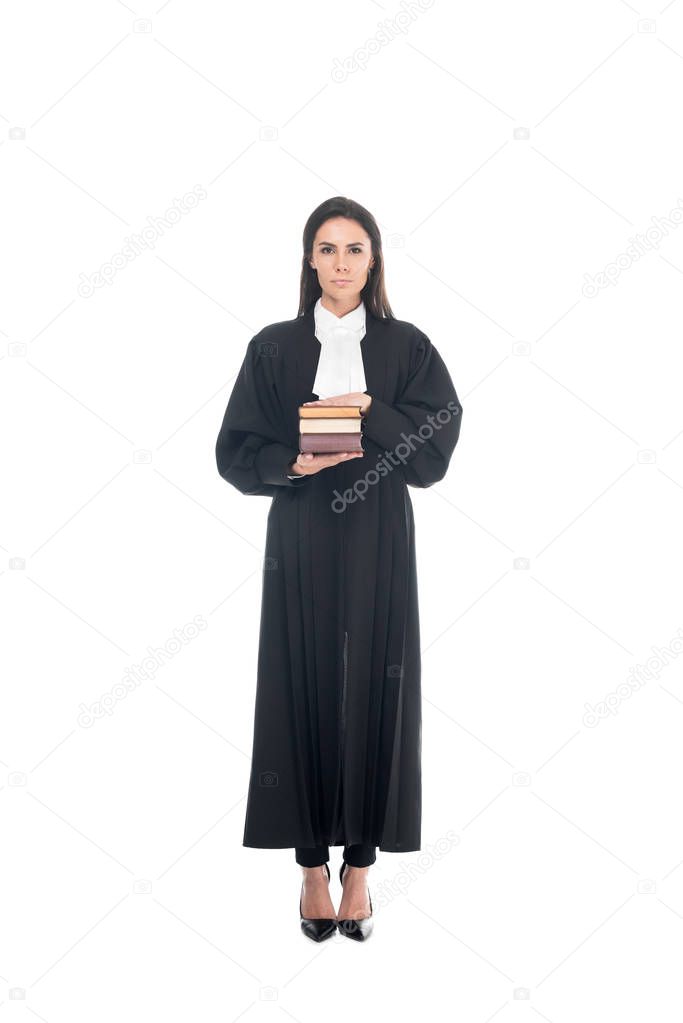 Full length view of serious judge in judicial robe holding books isolated on white