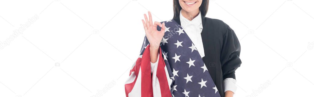 Panoramic shot of smiling judge holding american flag and showing okay sign isolated on white