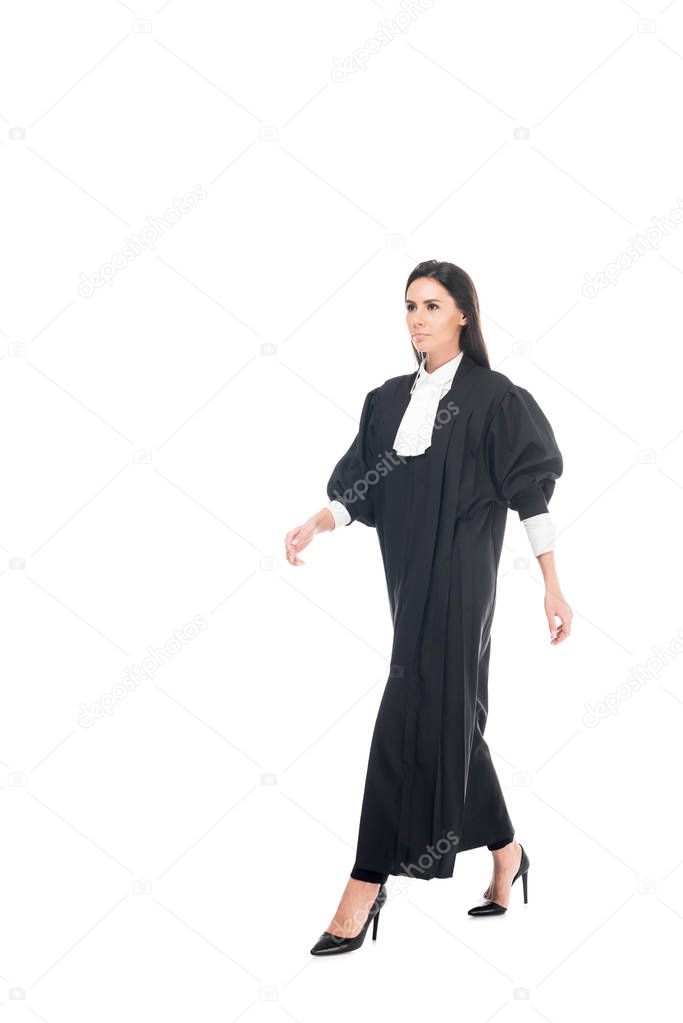 Full length view of serious judge in judicial robe walking isolated on white