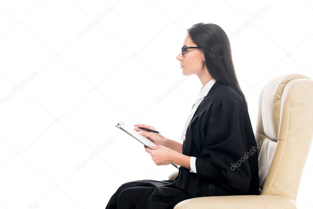 Side view of judge sitting in armchair and holding clipboard isolated on white