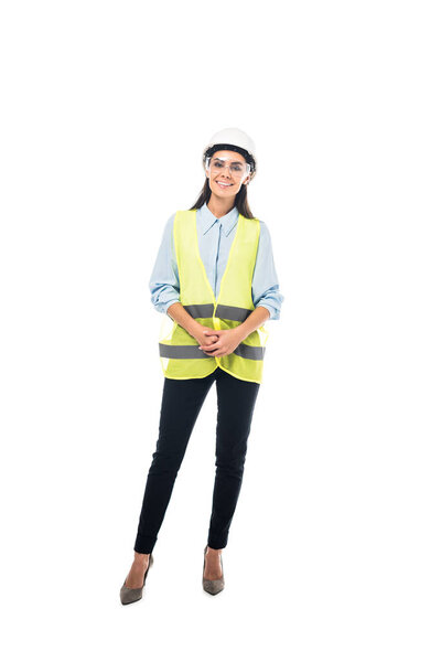 Full length view of smiling engineer in safety vest and hardhat isolated on white