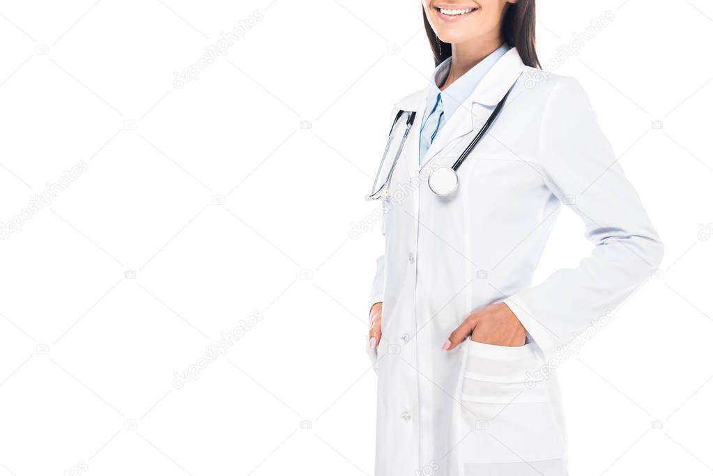 Cropped view of smiling doctor with stethoscope standing with hands in pockets isolated on white