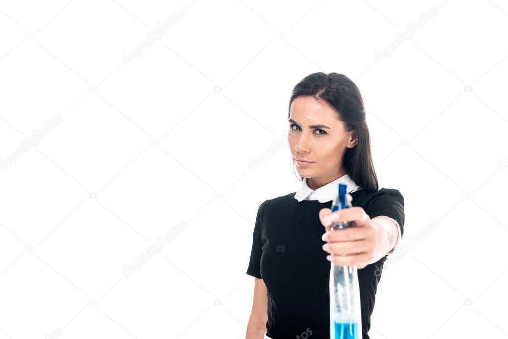 Confident maid in uniform holding spray bottle isolated on white