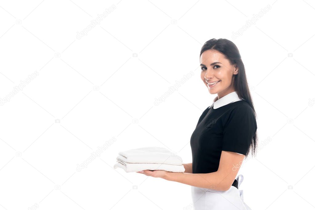 Smiling maid in uniform holding towels isolated on white