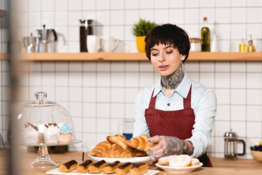 selective focus of beautiful barista standing near bar counter with tasty bakery clipart