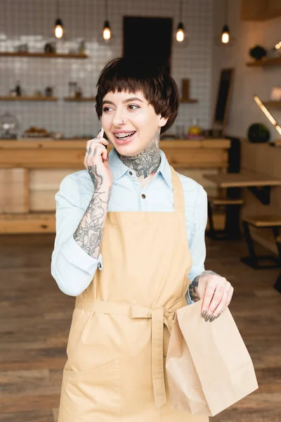 Smiling Waitress Apron Talking Smartphone Holding Paper Bag — Stock Photo, Image