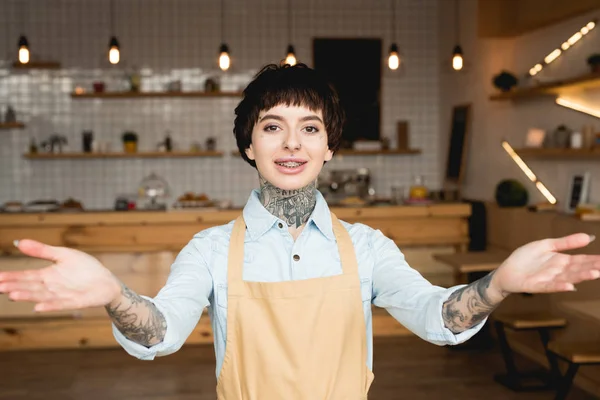 Hübsche Kellnerin Schürze Lächelt Zeigt Willkommensgeste Und Schaut Die Kamera — Stockfoto
