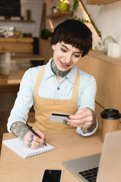 Camarera Sonriente Mirando Tarjeta Crédito Escribiendo Cuaderno —  Fotos de Stock