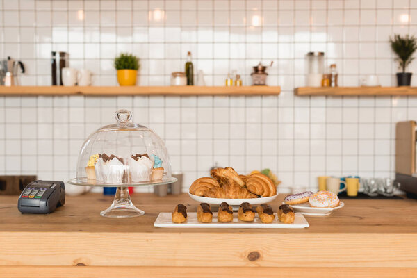bar counter with cake stand and dishes with delicious desserts and payment terminal