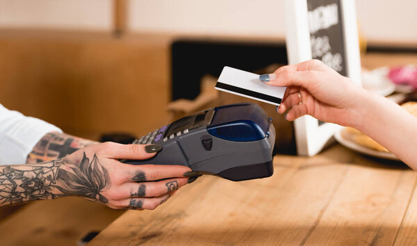 cropped view of customer holding credit card near payment terminal in cafe 