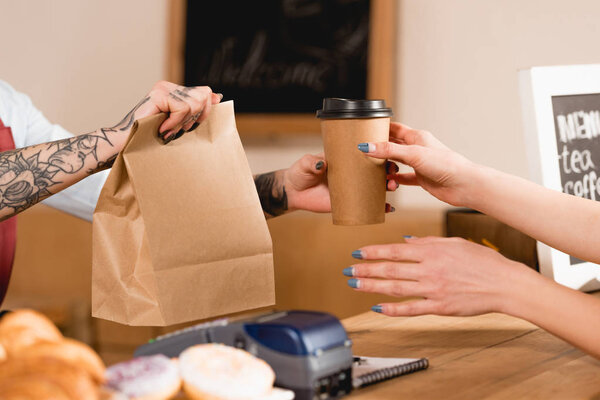 partial view of barista holding paper bag and disposable cup near customer