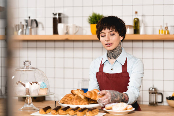 selective focus of beautiful barista standing near bar counter with tasty bakery
