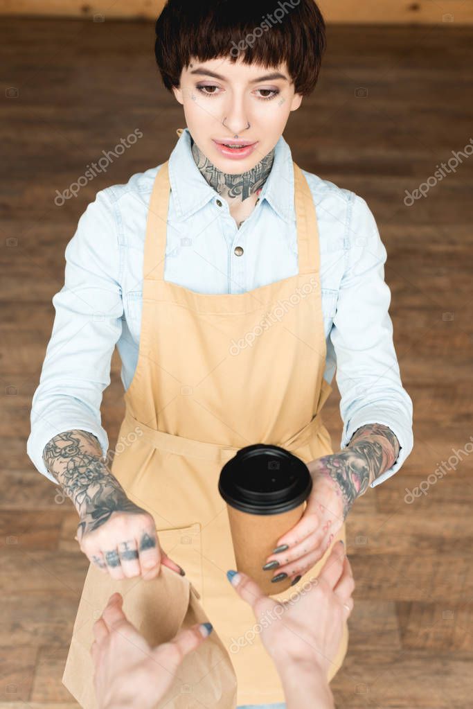 partial view of customer taking disposable cup and paper bag from smiling waitress