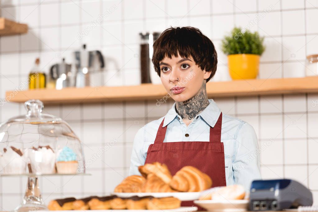 selective focus of pretty barista standing at bar counter with delicious pastry
