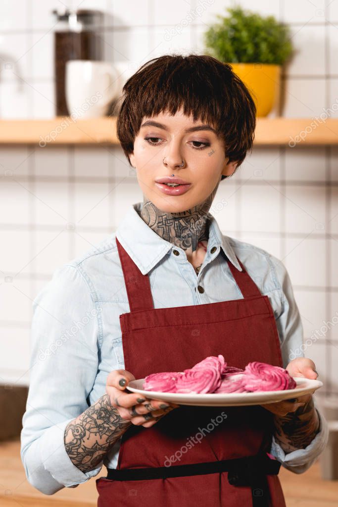 beautiful barista in apron holding dish with tasty cookies