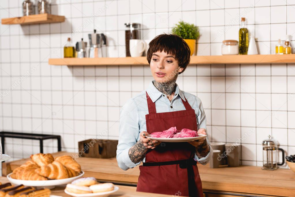 beautiful barista holding dish with tasty cookies while standing at bar counter in cafe 