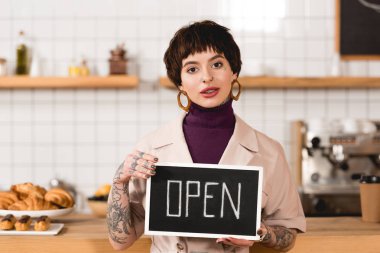 pretty businesswoman holding signboard with open lettering and looking at camera clipart
