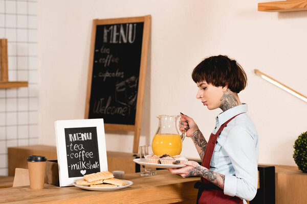pretty barista holding glass jug with juice while standing near bar counter