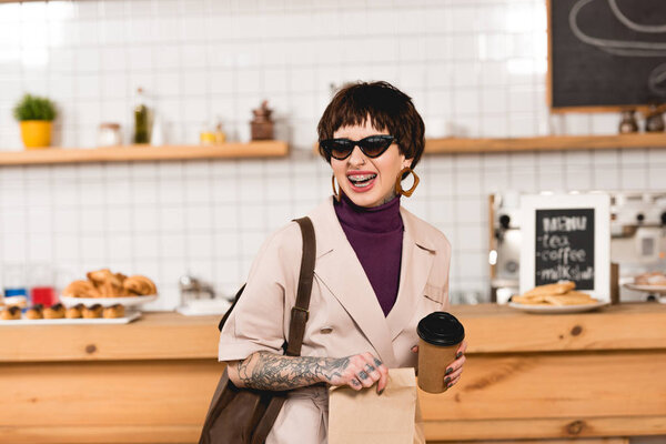 smiling, trendy businesswoman in sunglasses holding disposable cup