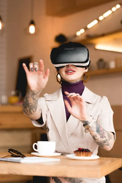 smiling businesswoman in virtual reality headset sitting at table in cafeteria
