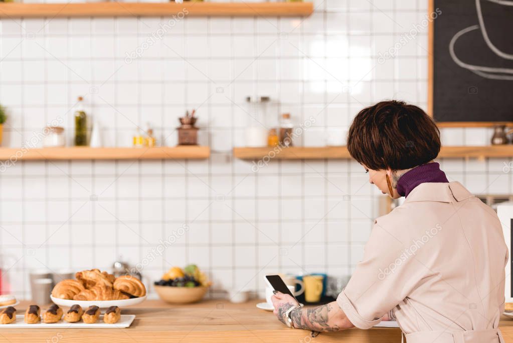 businesswoman holding smartphone while sitting at bar counter in cafeteria