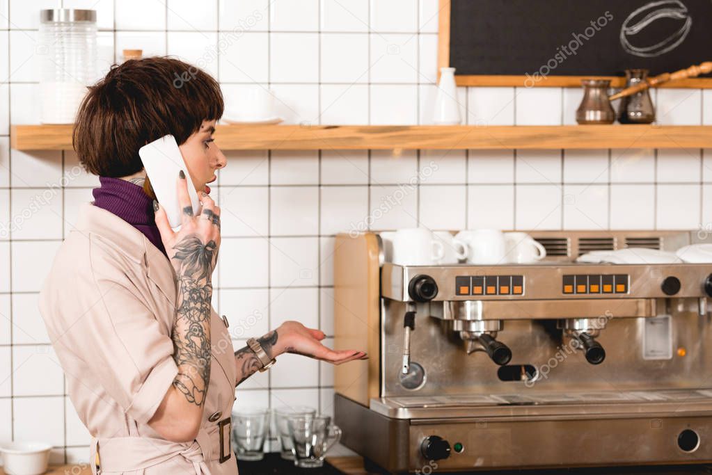 surprised businesswoman talking on smartphone while standing near espresso machine