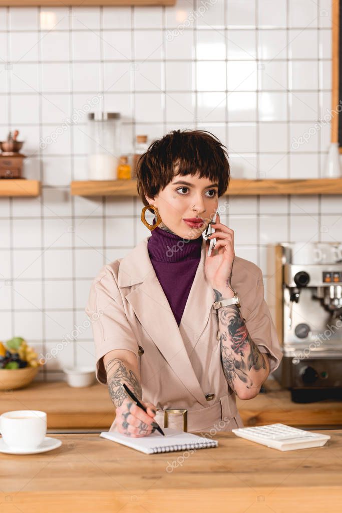 attractive businesswoman talking on smartphone while standing at bar counter in cafe
