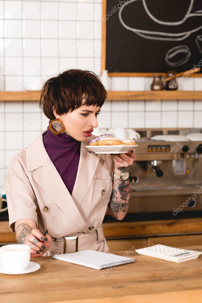 disgruntled businesswoman holding plate with macaroons while standing at bar counter in cafeteria