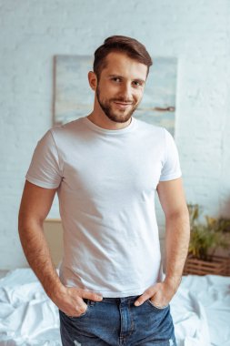 Elleri ceplerinde kameraya bakarak olan beyaz t-shirt, yakışıklı bir adam