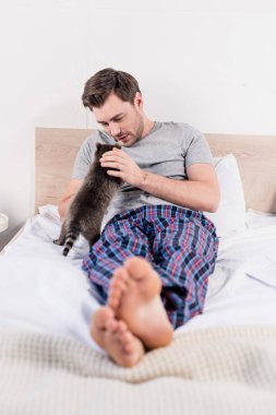 selective focus of handsome man in plaid shirt lying in bed with cute raccoon clipart