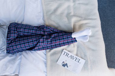 partial view of man in pyjamas lying on bed near travel newspaper clipart