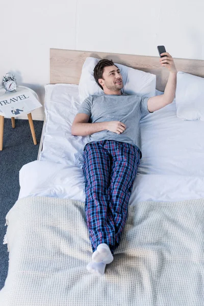 Bonito Homem Tomando Selfie Com Smartphone Enquanto Descansa Cama Casa — Fotografia de Stock